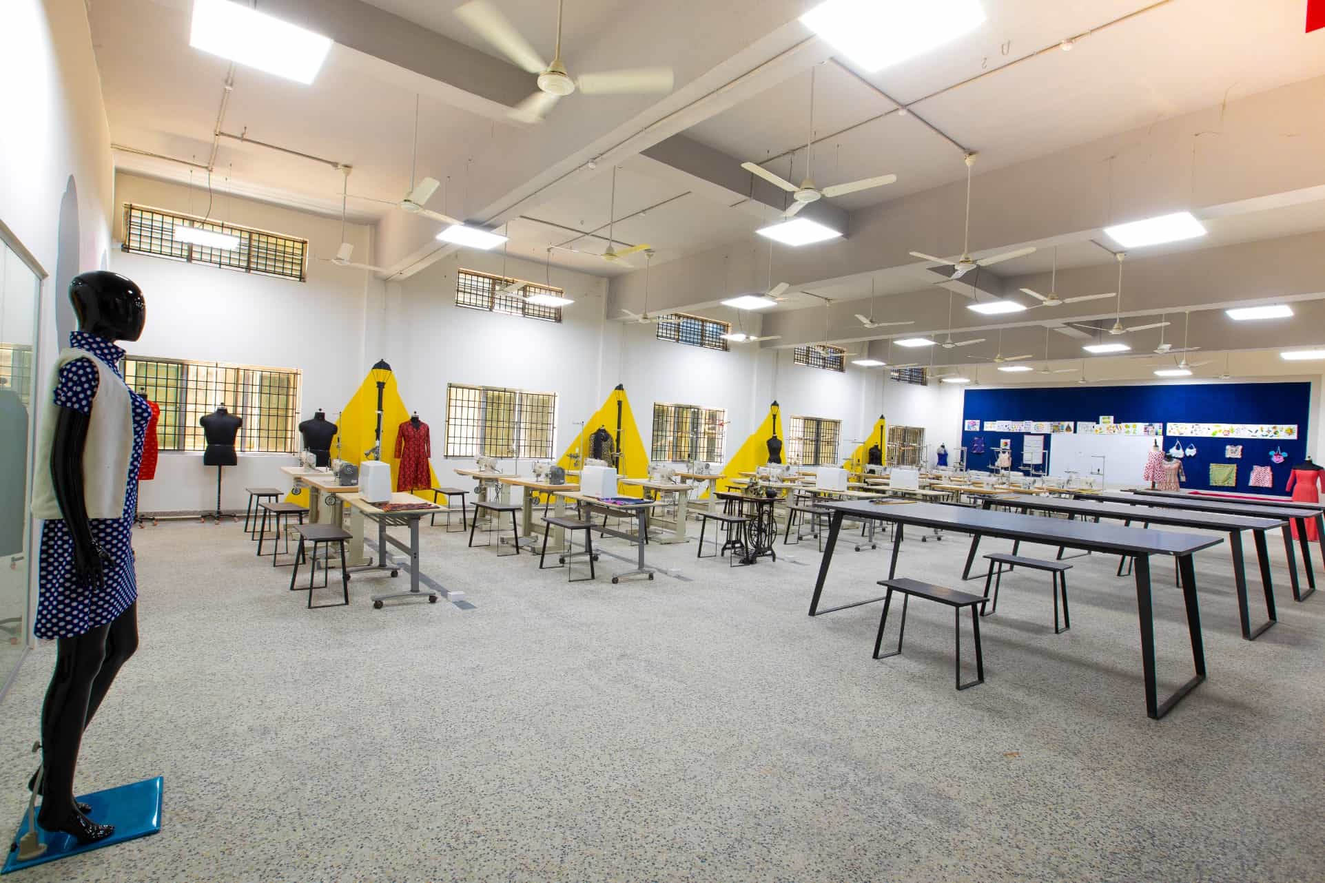 Spacious and well lit fashion design classroom with dressed mannequins and row of tables with sewing machines